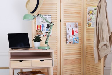 Photo of Folding screen, table, laptop and lamp indoors. Interior design