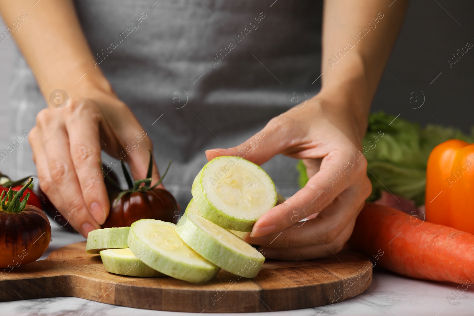 Photo of Cooking vegetable stew. Woman with cut zucchini and tomato at white marble table, closeup