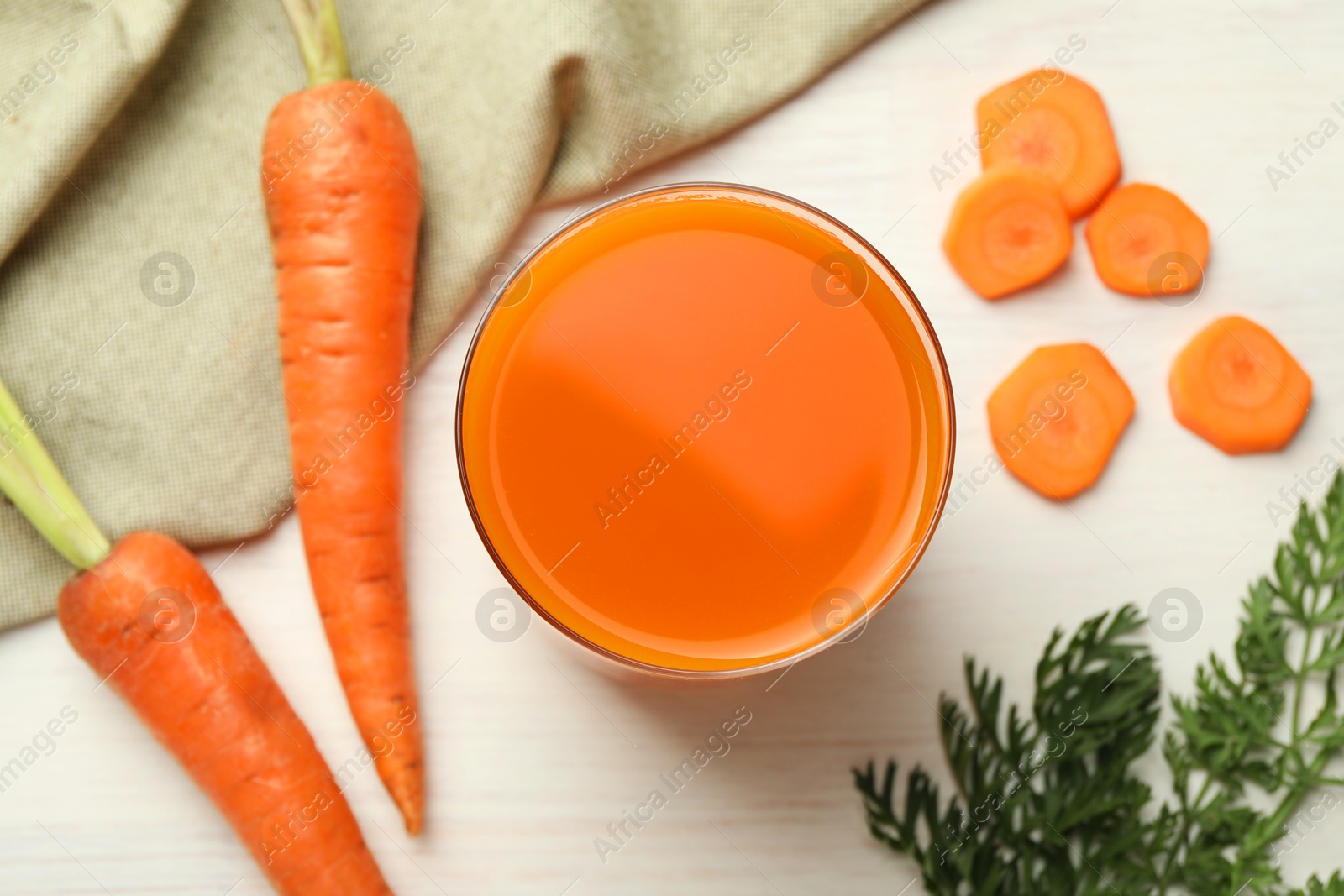 Photo of Fresh carrot juice in glass and vegetables on light wooden table, flat lay