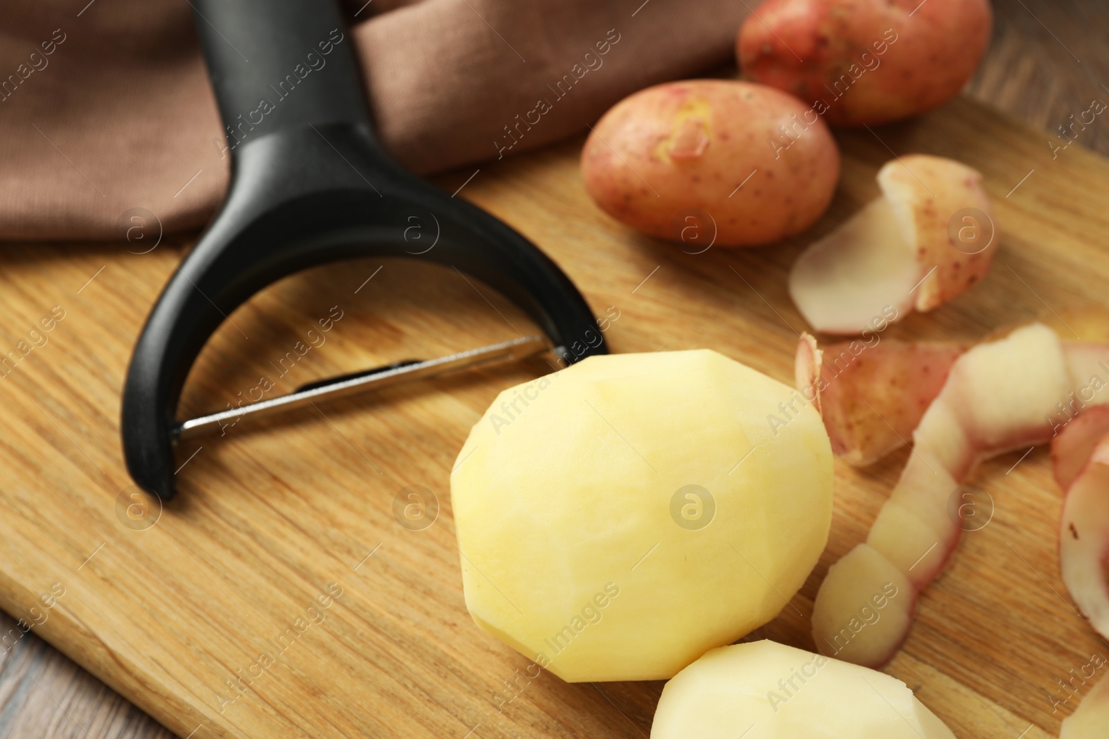 Photo of Fresh raw potatoes, peels and peeler on wooden table, closeup