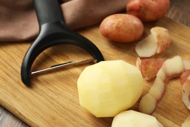 Photo of Fresh raw potatoes, peels and peeler on wooden table, closeup