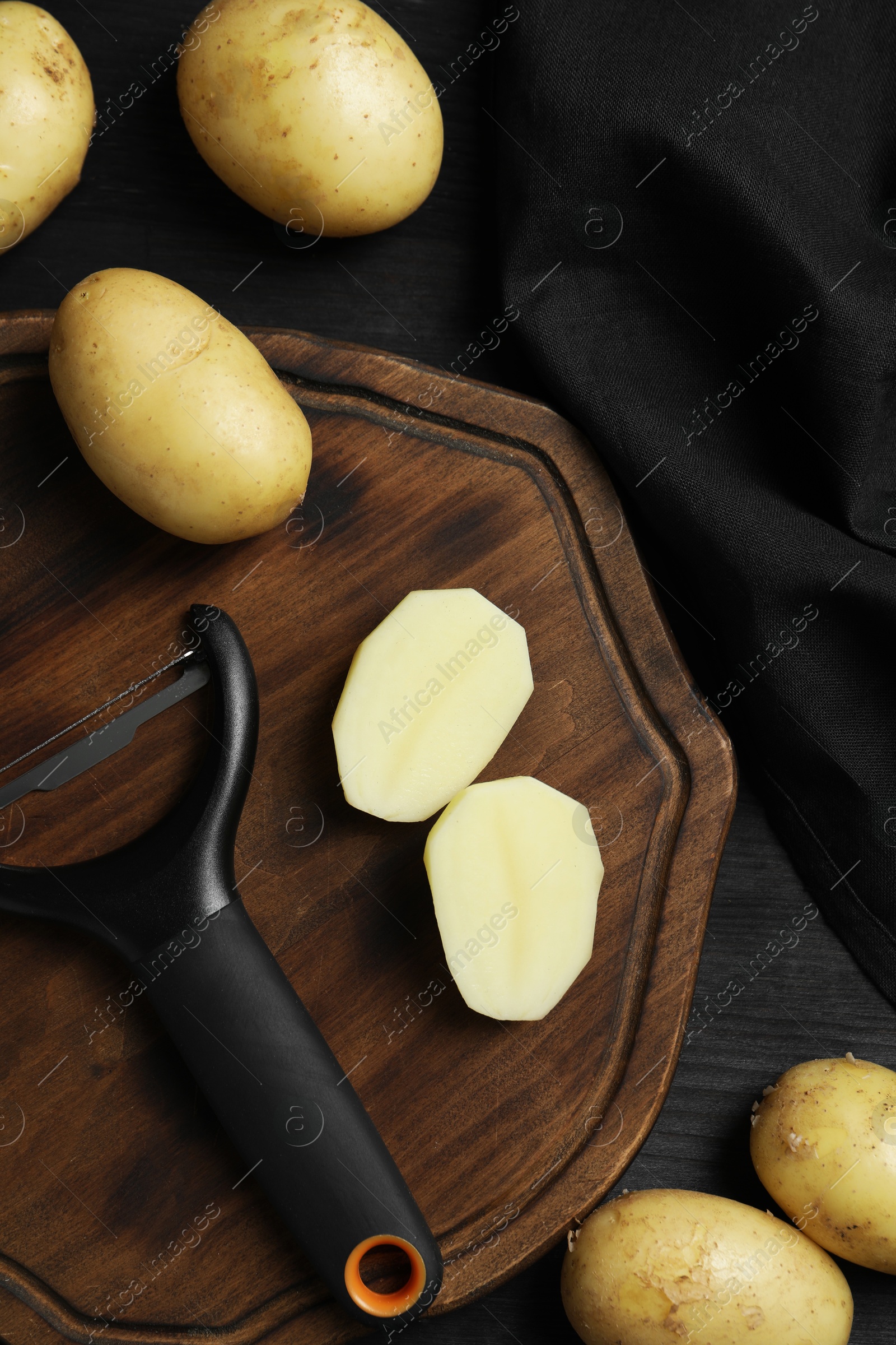 Photo of Fresh raw potatoes and peeler on black wooden table, flat lay