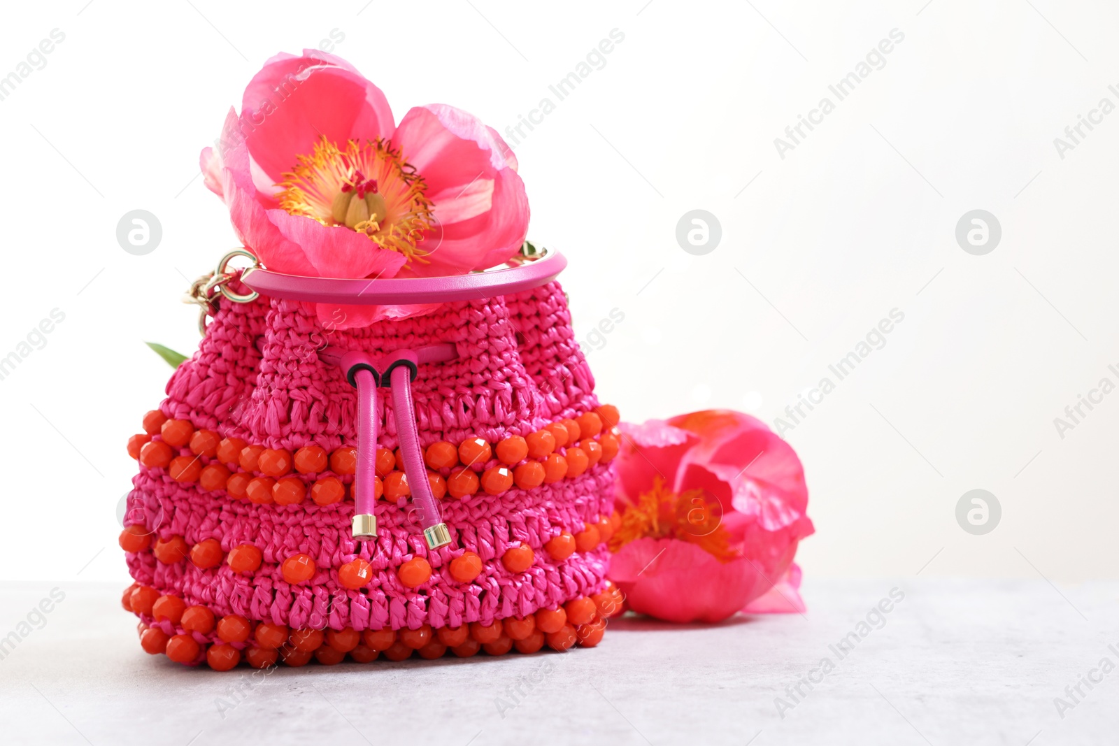 Photo of Stylish pink bag and peony flowers on gray table against light background, space for text