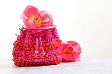 Photo of Stylish pink bag and peony flowers on gray table against light background, space for text