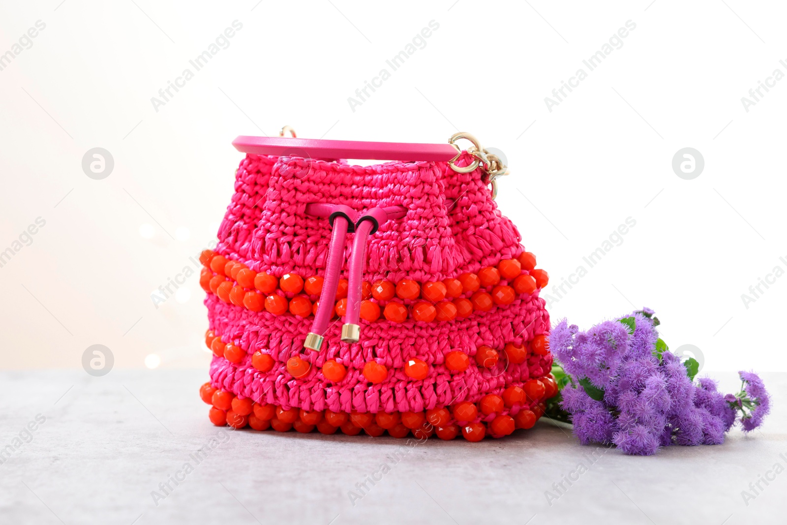 Photo of Stylish pink bag and ageratum flowers on gray table against light background