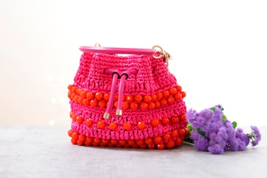 Photo of Stylish pink bag and ageratum flowers on gray table against light background