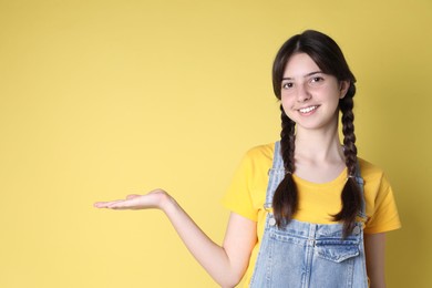 Portrait of smiling teenage girl holding something on yellow background. Space for text