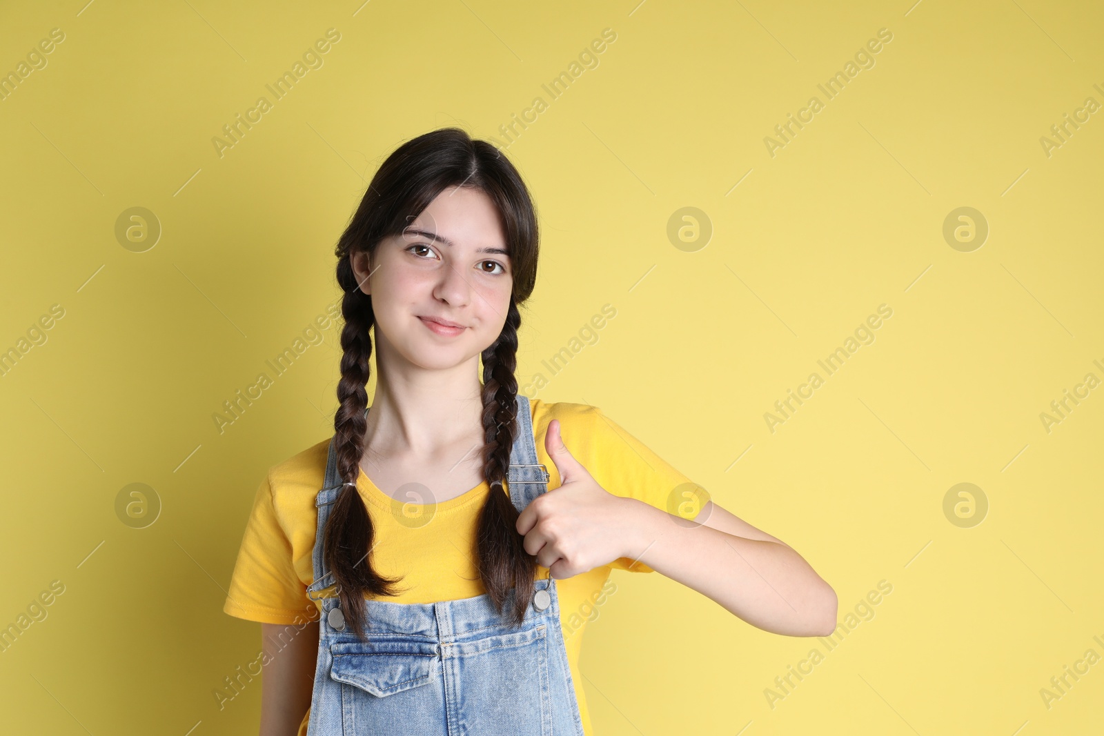 Photo of Portrait of cute teenage girl showing thumbs up on yellow background