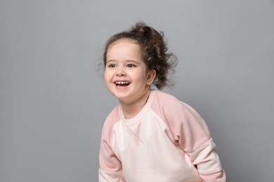 Photo of Adorable child. Portrait of happy girl on grey background. Space for text