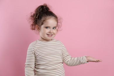 Photo of Adorable child. Portrait of smiling girl showing something on pink background