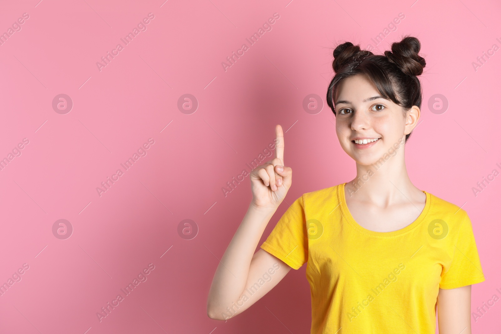 Photo of Portrait of smiling teenage girl pointing at something on pink background. Space for text