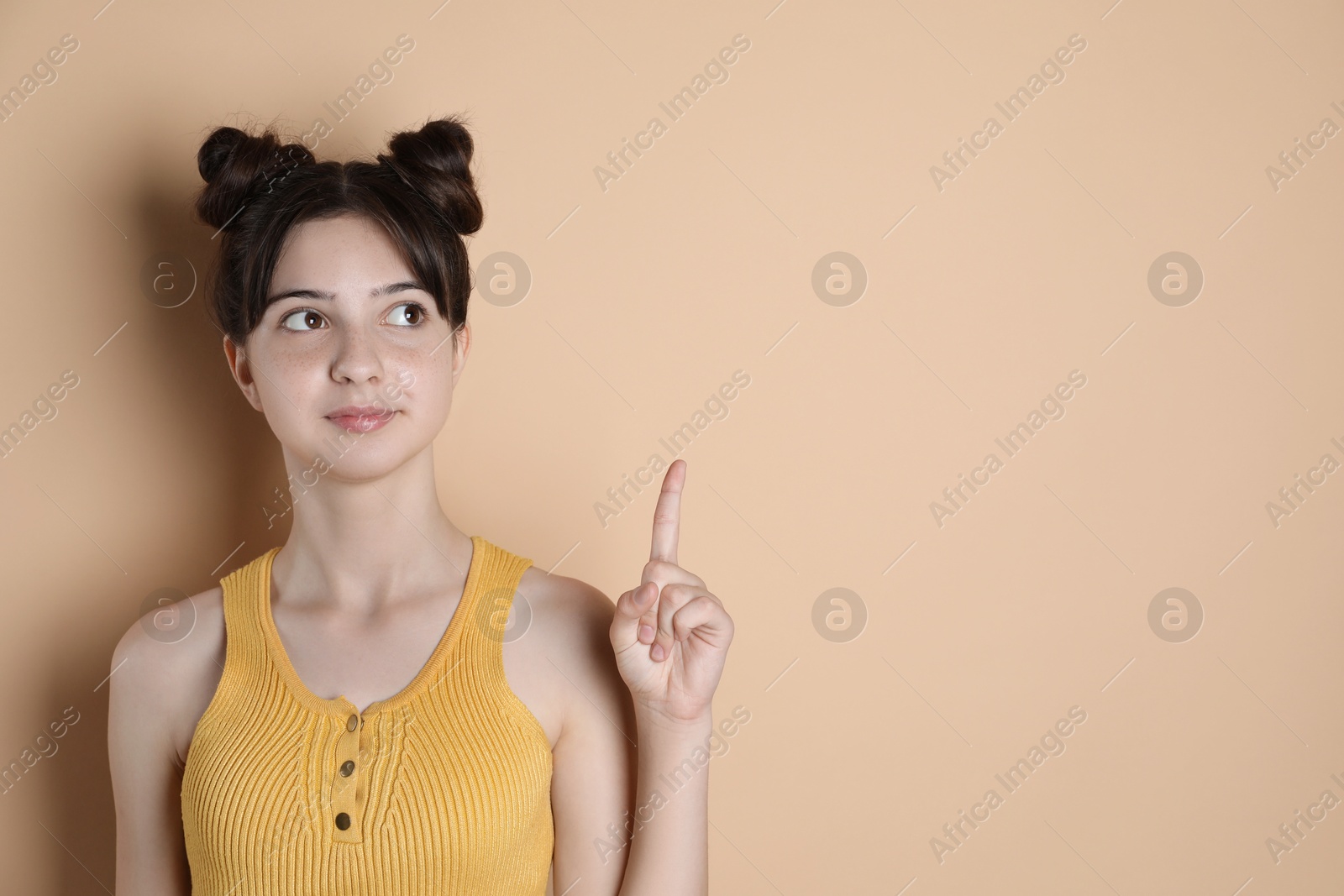 Photo of Portrait of cute teenage girl pointing at something on beige background. Space for text