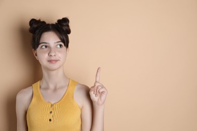 Photo of Portrait of cute teenage girl pointing at something on beige background. Space for text