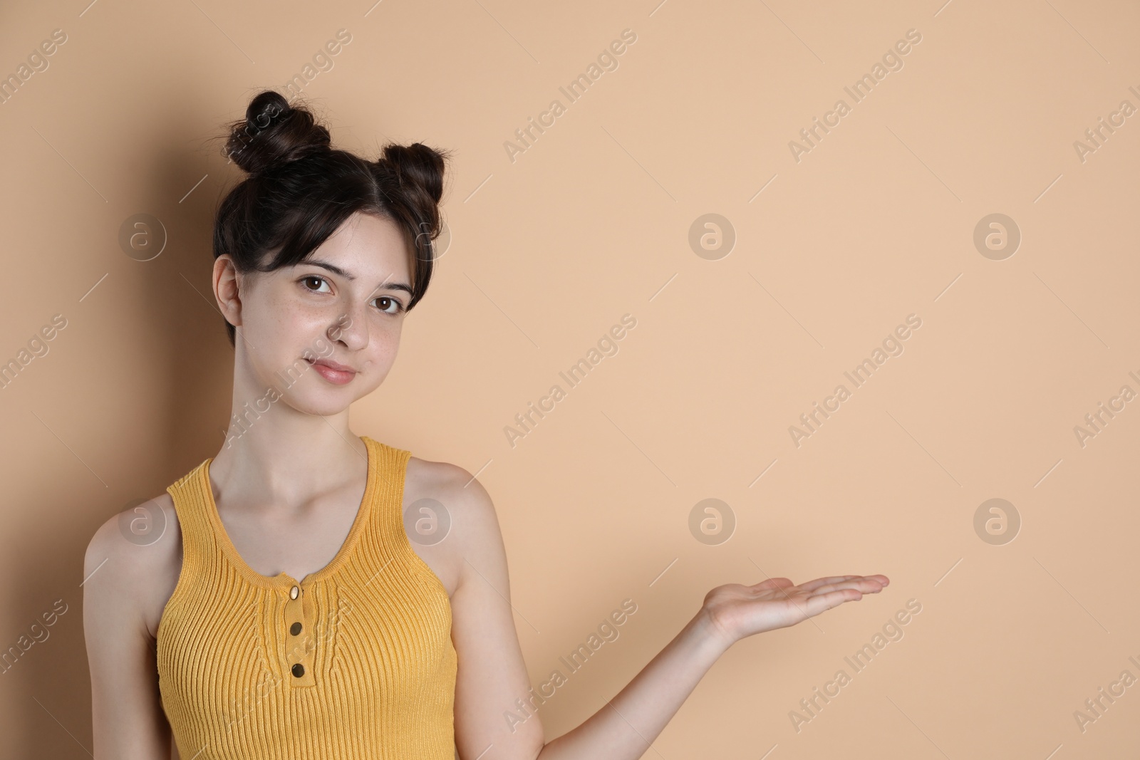 Photo of Portrait of cute teenage girl showing something on beige background. Space for text