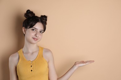 Photo of Portrait of cute teenage girl showing something on beige background. Space for text