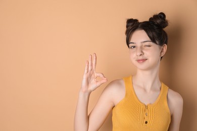 Portrait of cute teenage girl showing ok gesture on beige background. Space for text