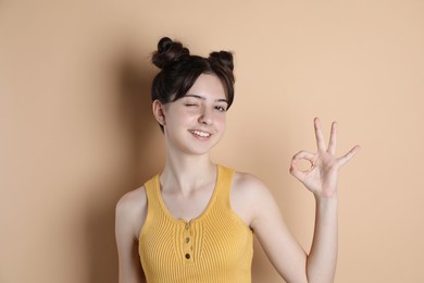 Portrait of smiling teenage girl showing ok gesture on beige background