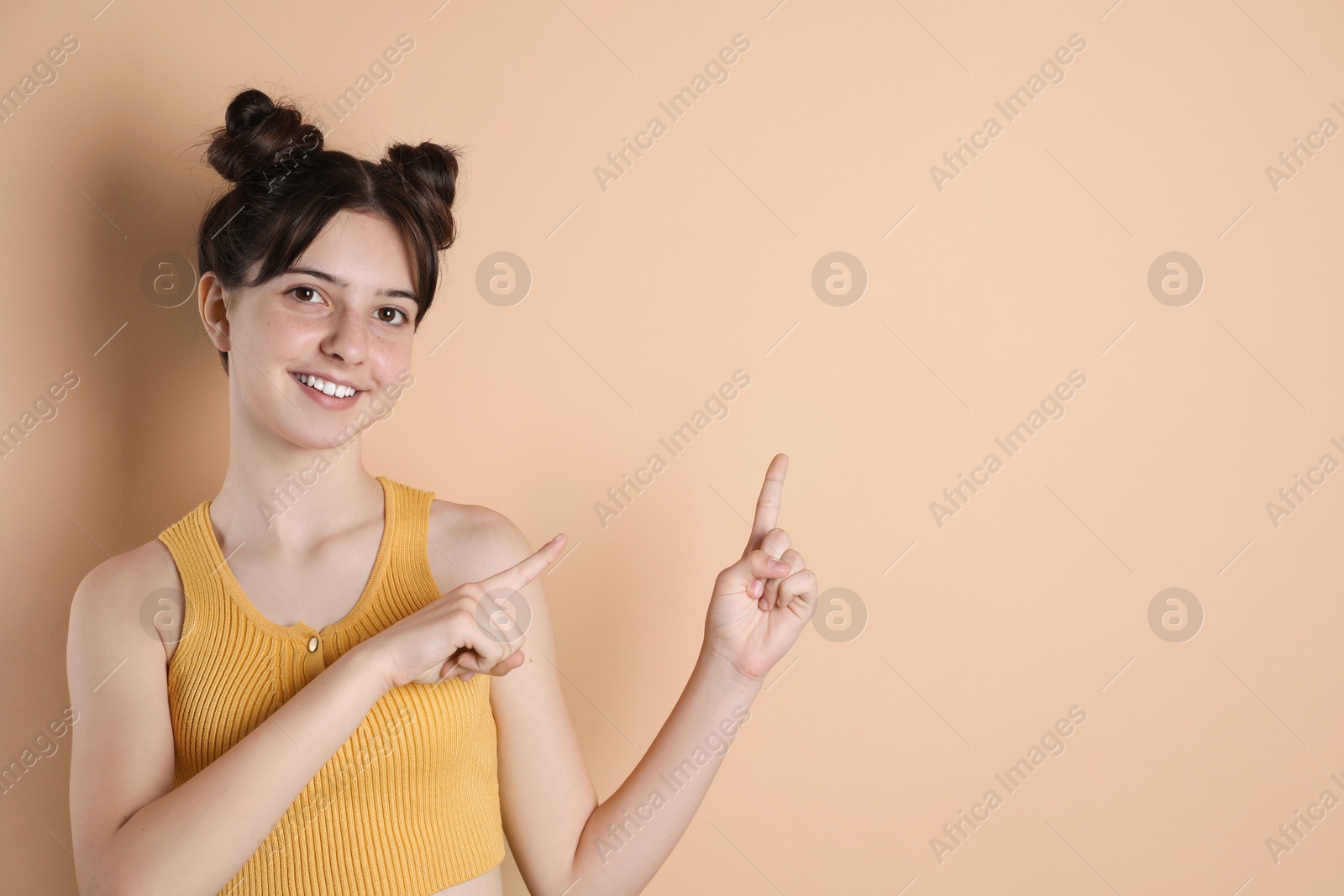 Photo of Portrait of smiling teenage girl pointing at something on beige background. Space for text