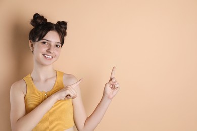 Portrait of smiling teenage girl pointing at something on beige background. Space for text