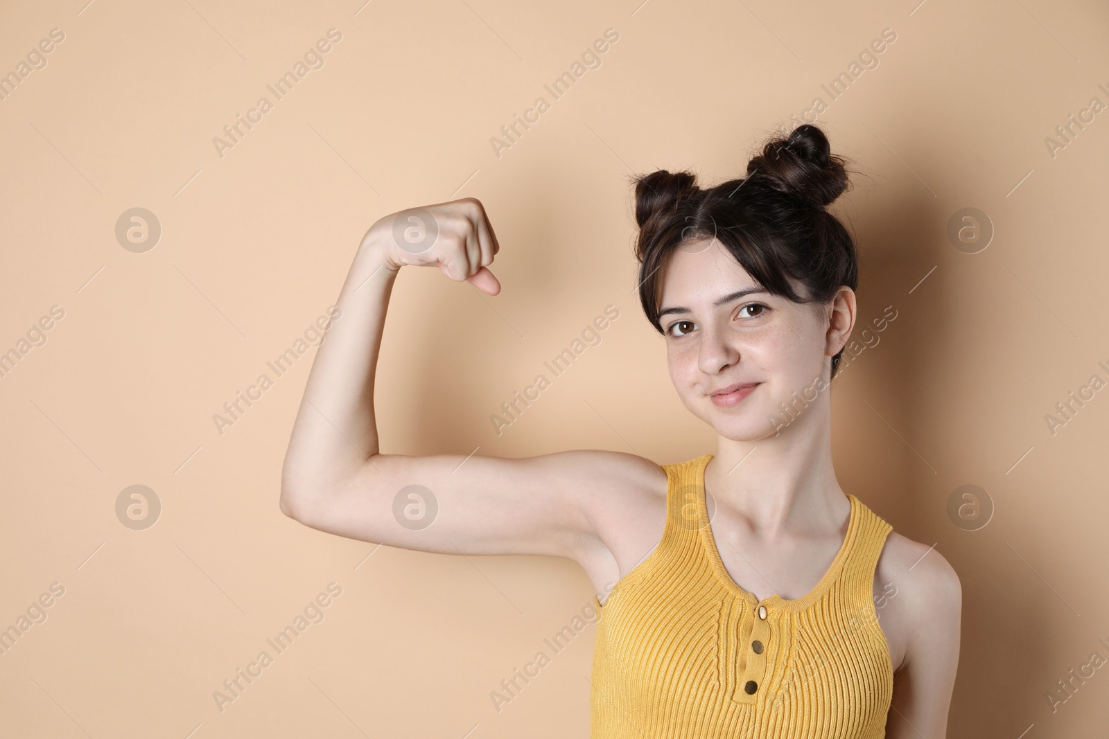 Photo of Portrait of cute teenage girl showing muscles on beige background. Space for text