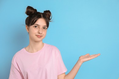 Portrait of cute teenage girl holding something on light blue background. Space for text