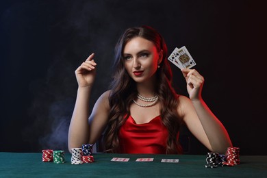 Charming woman playing poker at table on black background with smoke