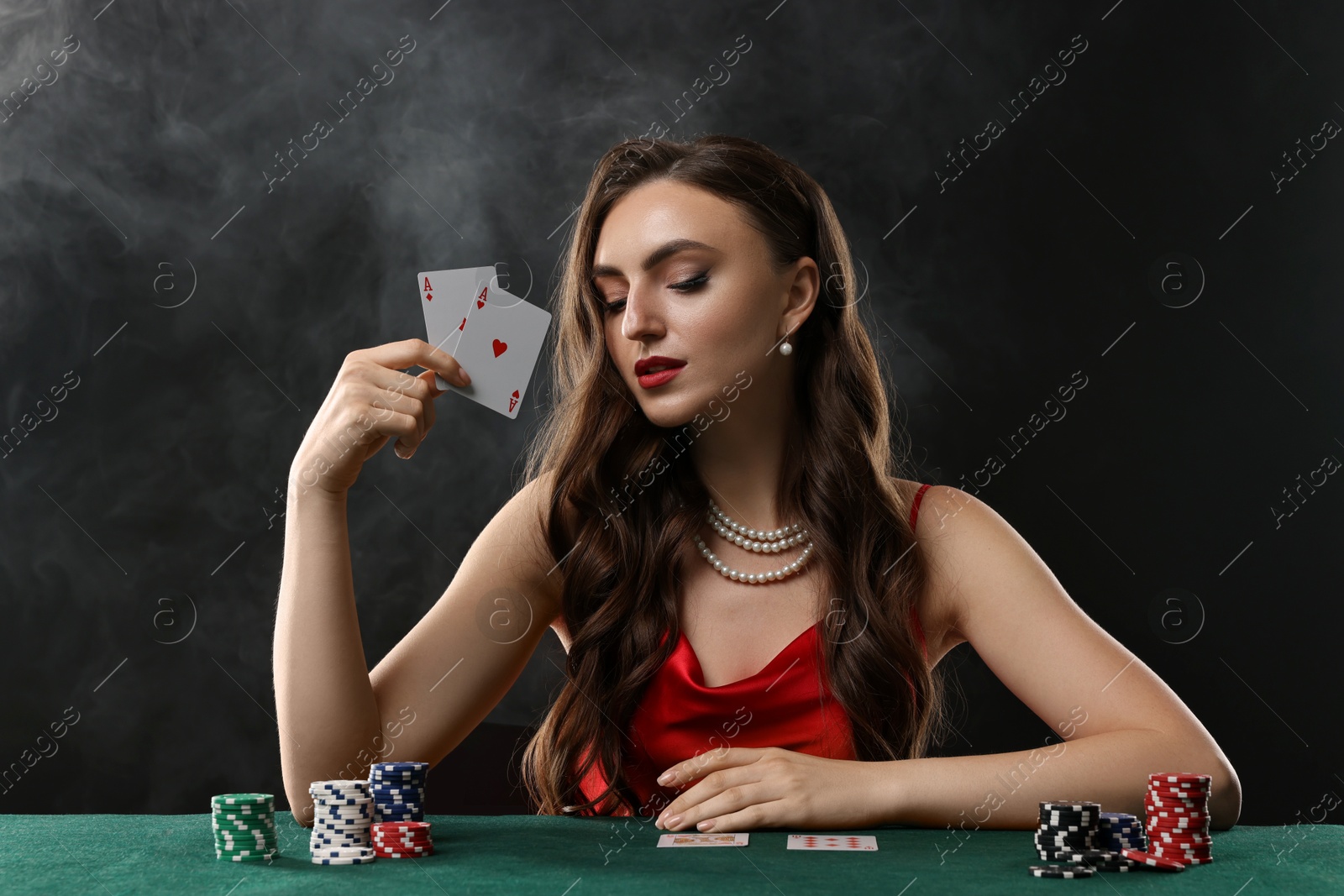 Photo of Charming woman playing poker at table on black background with smoke