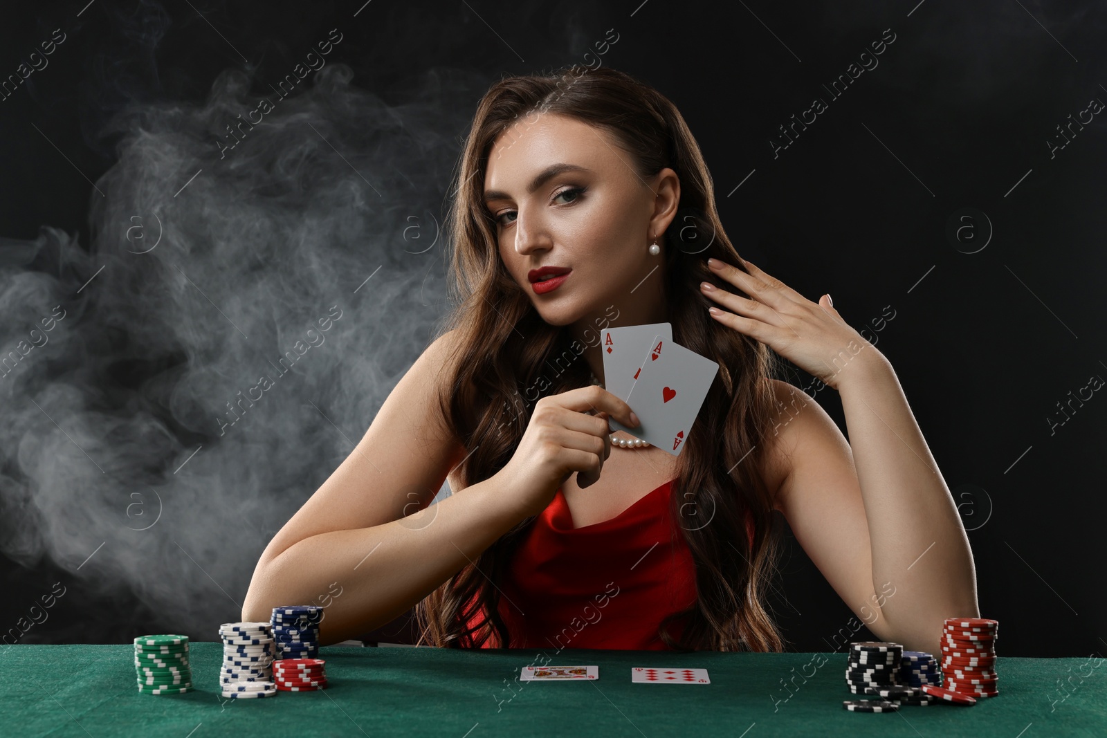 Photo of Charming woman playing poker at table on black background with smoke