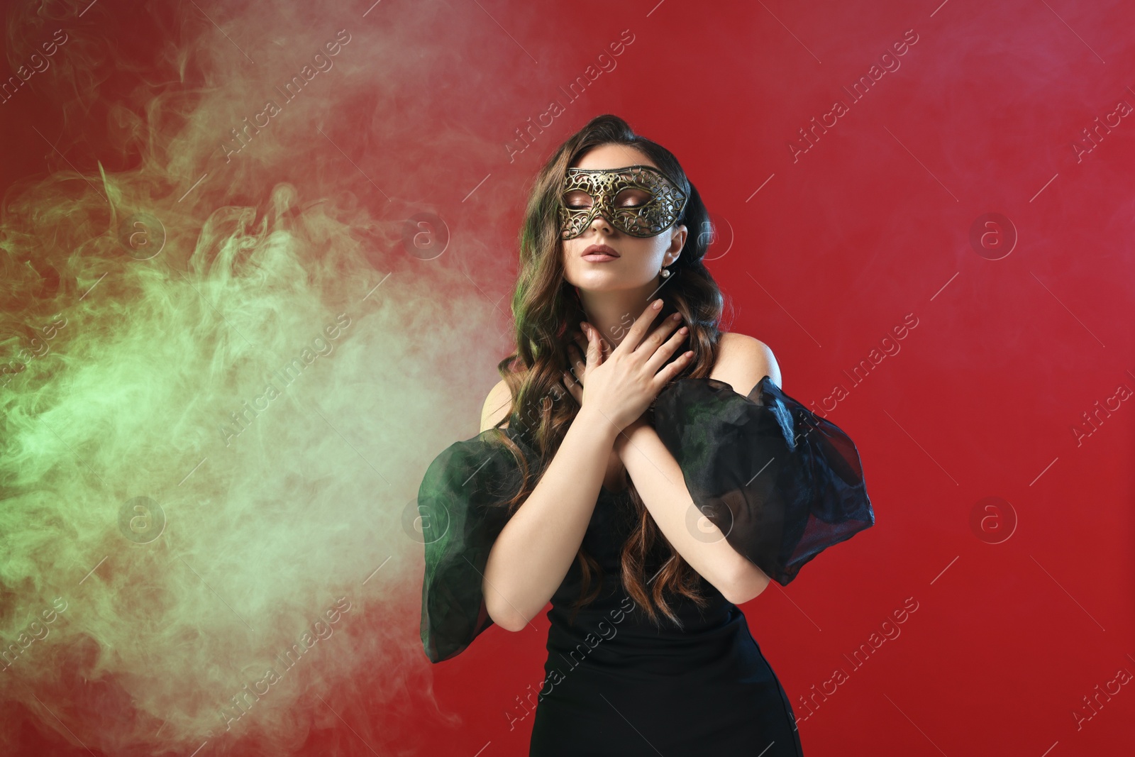 Photo of Beautiful woman wearing carnival mask on red background in color lights and smoke