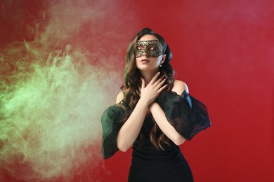 Photo of Beautiful woman wearing carnival mask on red background in color lights and smoke