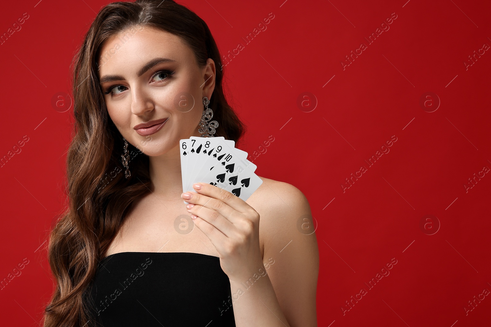 Photo of Poker game. Charming woman with playing cards on red background. Space for text