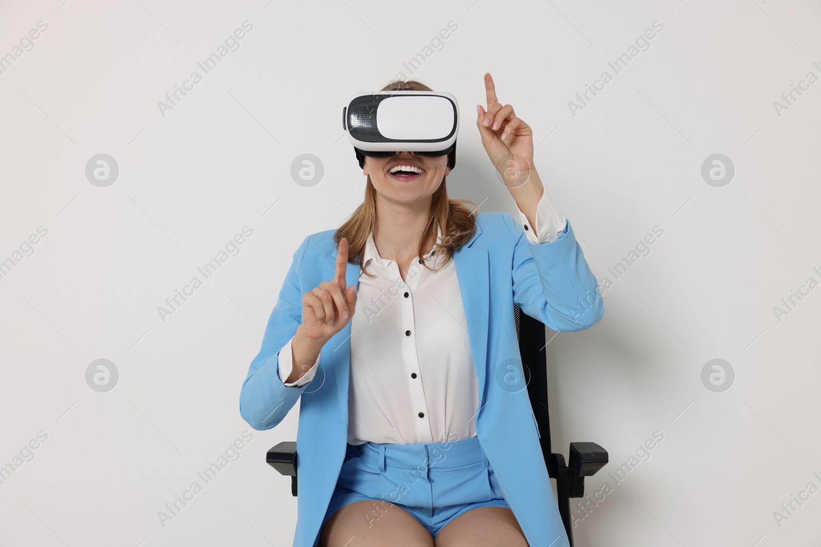 Photo of Happy woman with virtual reality headset sitting on chair against white background