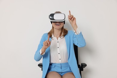 Happy woman with virtual reality headset sitting on chair against white background