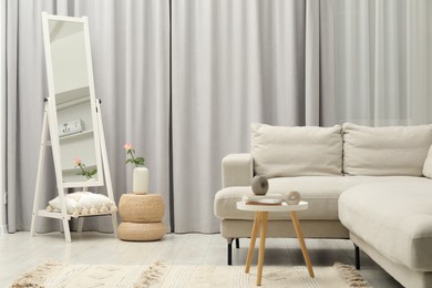 Photo of Beautiful mirror, side table, decorative elements and sofa in stylish living room