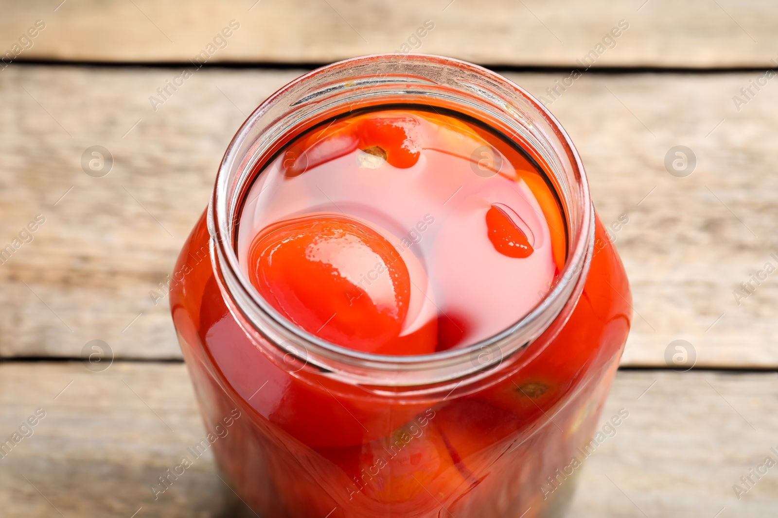 Photo of Tasty pickled tomatoes in jar on wooden table, closeup