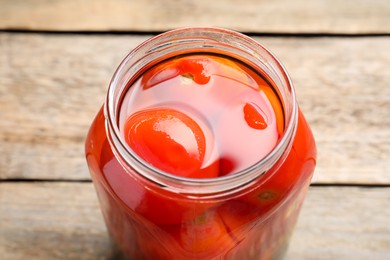 Tasty pickled tomatoes in jar on wooden table, closeup