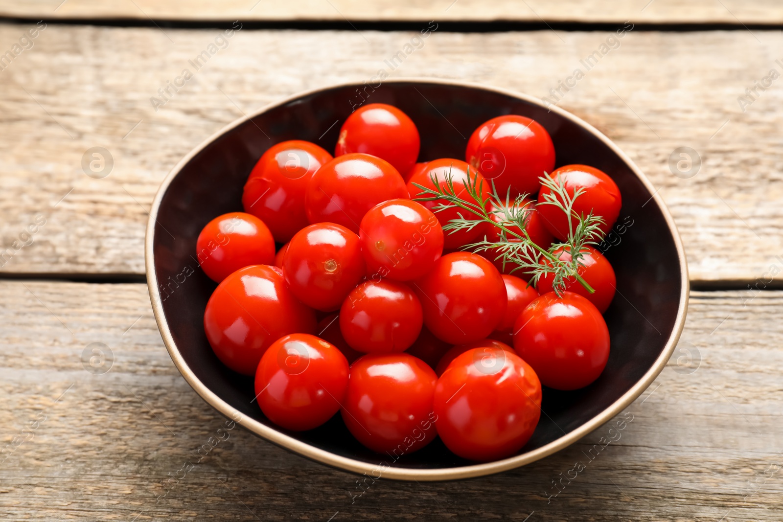 Photo of Tasty pickled tomatoes and dill in bowl on wooden table