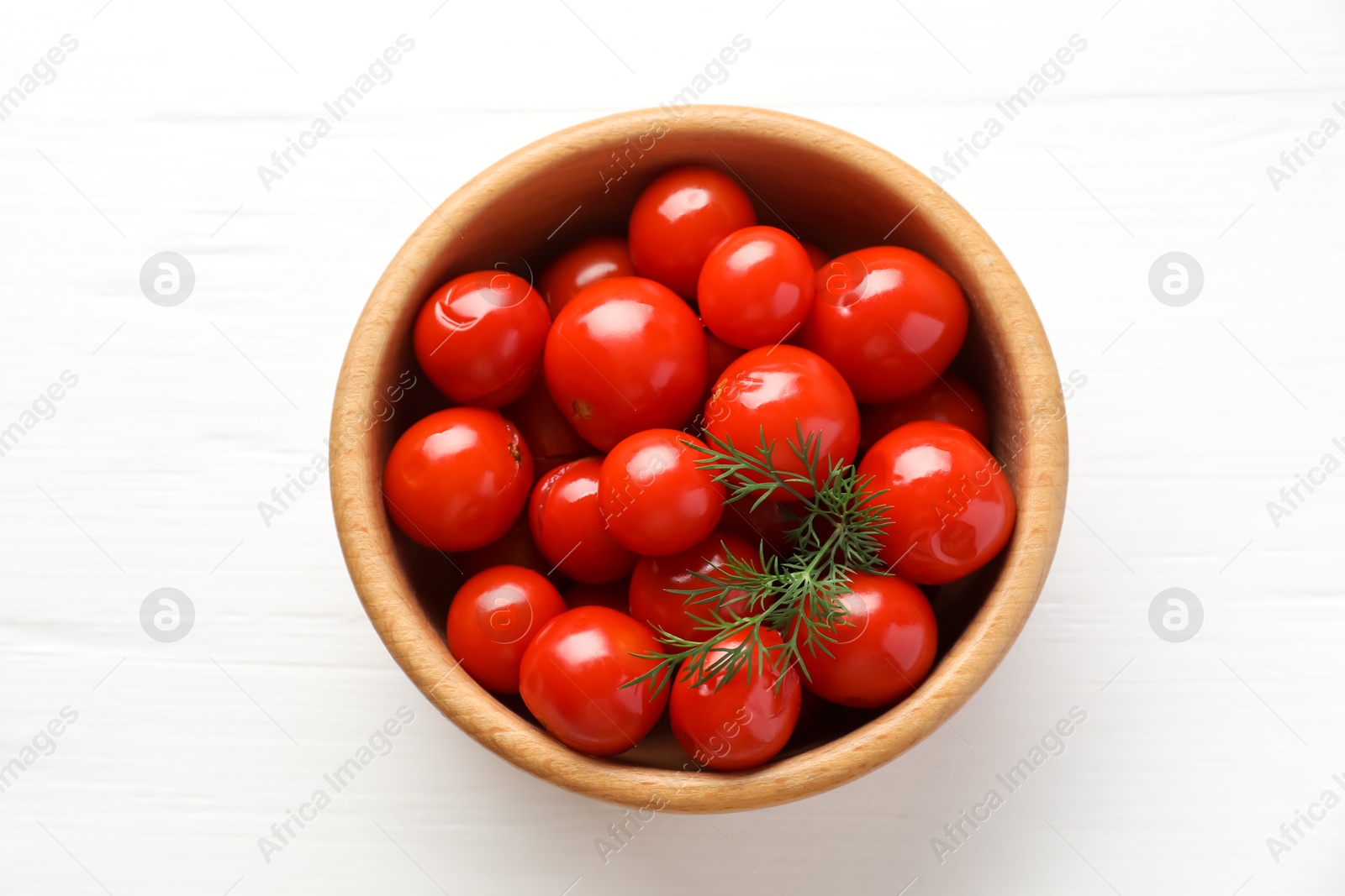 Photo of Tasty pickled tomatoes and dill in bowl on white wooden table, top view