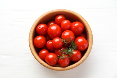 Photo of Tasty pickled tomatoes and dill in bowl on white wooden table, top view