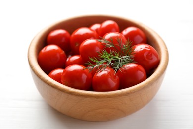 Tasty pickled tomatoes and dill in bowl on white wooden table, closeup