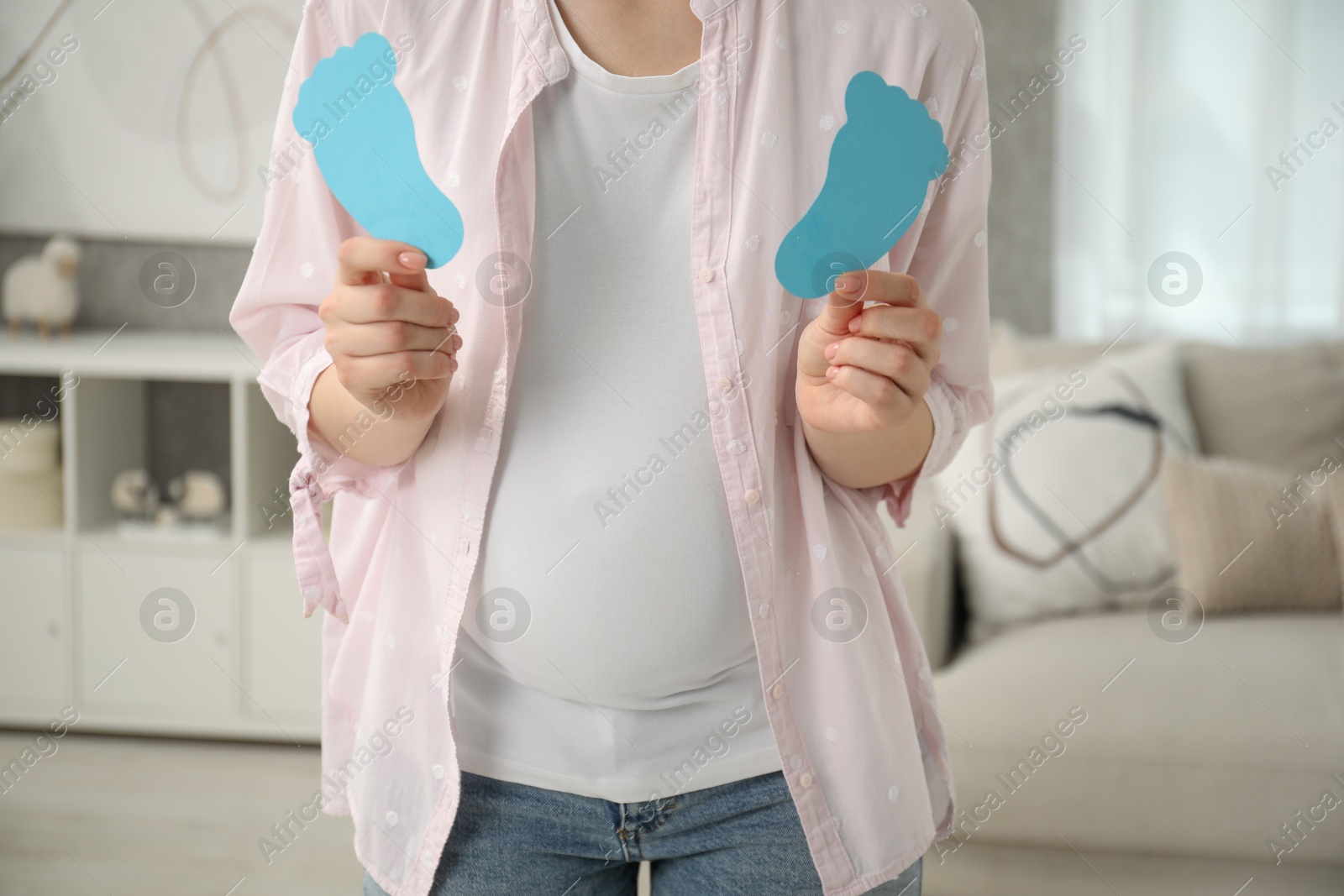 Photo of Expecting twins. Pregnant woman holding two paper cutouts of feet at home, closeup