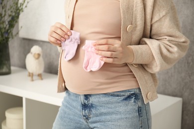 Expecting twins. Pregnant woman holding two pairs of socks at home, closeup