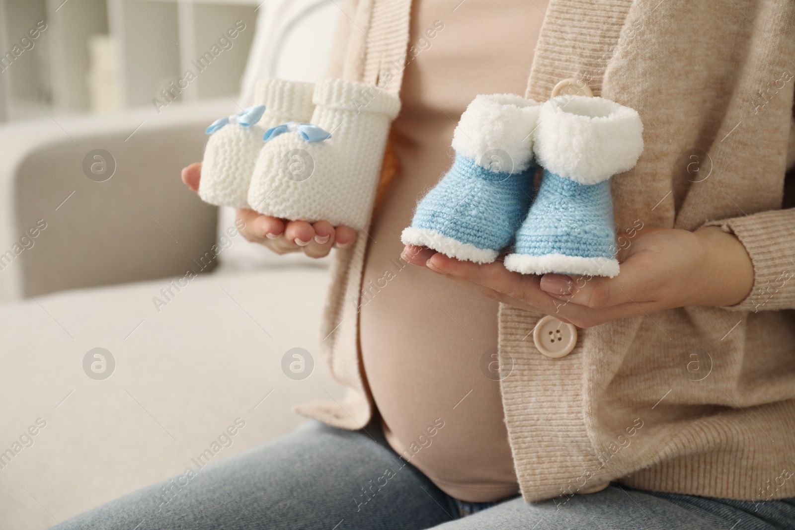 Photo of Expecting twins. Pregnant woman holding two pairs of shoes at home, closeup