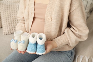 Expecting twins. Pregnant woman holding two pairs of shoes at home, closeup