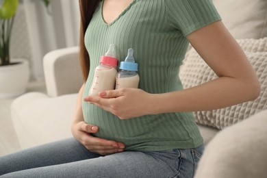 Expecting twins. Pregnant woman holding two bottles of milk at home, closeup