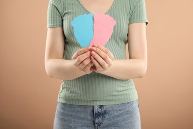 Expecting twins. Pregnant woman holding two paper cutouts of feet on light brown background, closeup