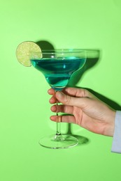 Photo of Woman with glass of refreshing cocktail on green background, closeup