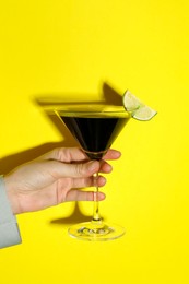 Photo of Woman with glass of refreshing cocktail on yellow background, closeup