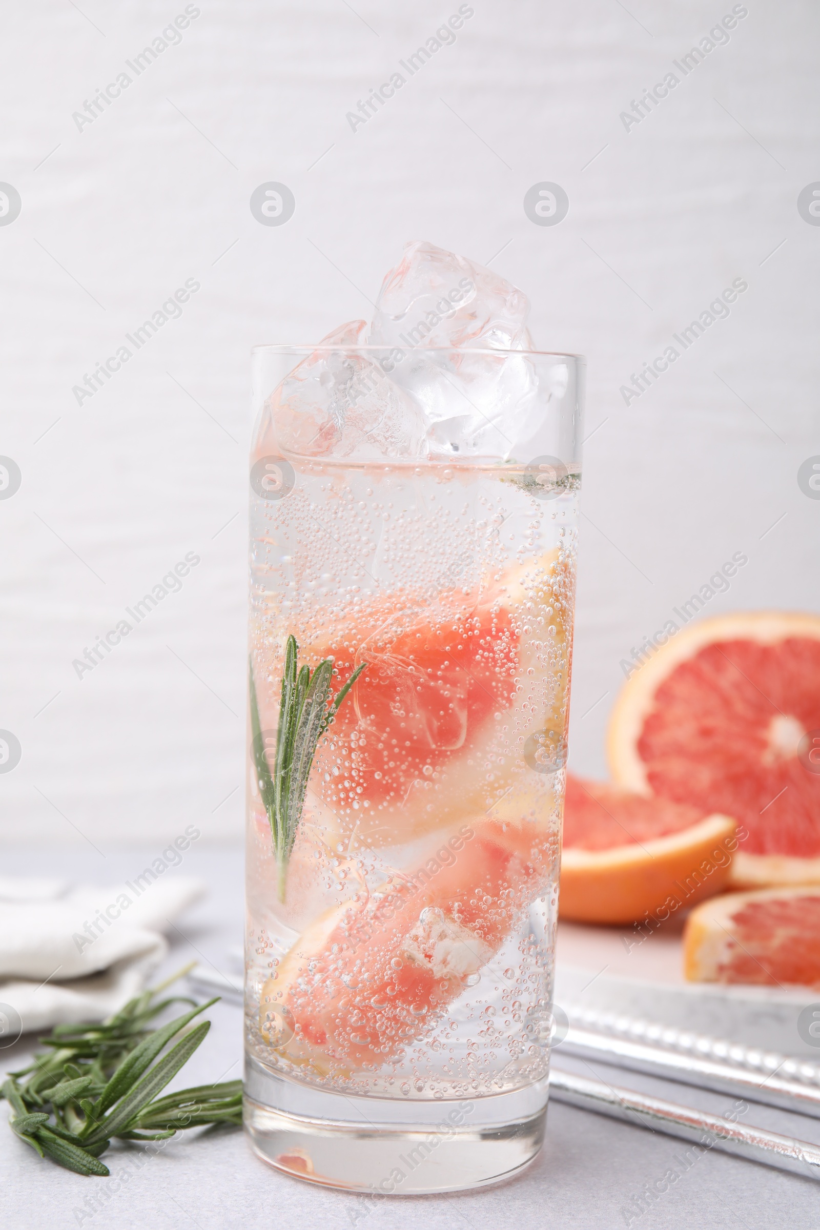 Photo of Refreshing water with grapefruit and rosemary in glass on light table