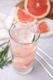 Refreshing water with grapefruit and rosemary in glass on light table, closeup